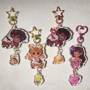 Może przedstawiać: Cztery akrylowe breloczki do kluczy z postaciami z kreskówek. Każdy breloczek ma inny wzór, w tym postać z workiem pieniędzy, postać ze skrzydłami, postać w okularach i postać z kwiatem. Breloczki mają złote i różowe okucia.