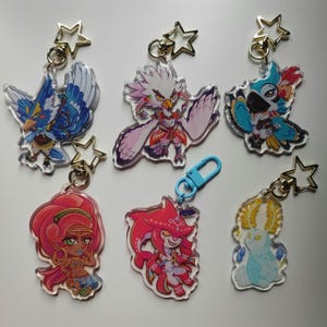 May include: Six colorful character keychains with gold star charms. The characters include a blue bird, a white bird, a blue parrot, a red-haired woman, a red fish, and a white creature with horns.