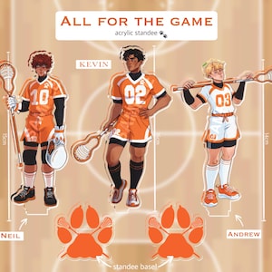 May include: Three acrylic standees titled All For The Game featuring characters Neil, Kevin, and Andrew in orange and white sports uniforms with lacrosse sticks. Heights are marked as 15cm, 16cm, and 14cm. Includes two orange paw-shaped standee bases.