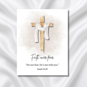 Op de afbeelding: Een print in aquarel-stijl met een houten kruis, gedrapeerd met een witte doek. De tekst "Faith over fear" staat boven de quote "Wees niet bevreesd, want Ik ben met u" uit Jesaja 41:10. De achtergrond is zacht en neutraal van kleur.