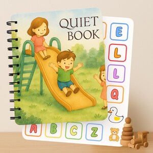 Op de afbeelding: Een spiraalgebonden "Quiet Book" met een kleurrijke illustratie van kinderen die op een glijbaan spelen. De kaft toont de tekst "QUIET BOOK". Extra pagina's tonen letters, een eend, een teddybeer, een houten stapelspeelgoed en een houten trein.