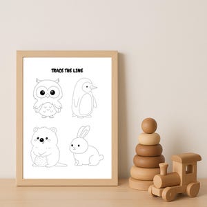 Op de afbeelding: Een ingelijste print met de tekst "TRACE THE LINE" boven vier omtrek tekeningen van dieren: een uil, een pinguïn, een hamster en een konijn. Een houten stapelspeelgoed en een houten trein staan rechts.