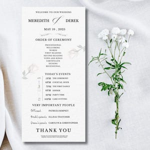 Op de afbeelding: Een trouwprogramma met de namen Meredith en Derek, gedateerd 10 mei 2025. Het programma bevat de volgorde van de ceremonie, de evenementen van vandaag en belangrijke personen. Witte bloemen rechts.