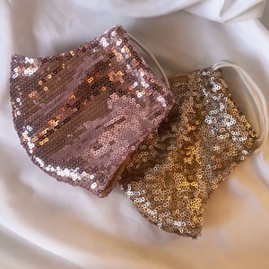 May include: Two face masks made of sequins. One is rose gold and the other is gold.