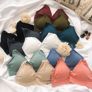 May include: A collection of 10 different colored and styled bras, all laid out on a white surface. The bras are made of a soft, stretchy material and have a variety of strap styles.