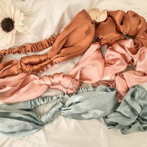 May include: Four satin headbands in different colors and patterns. The headbands are tied in a knot and are lying on a white surface. The headbands are in the colors of light blue, pink, and brown.