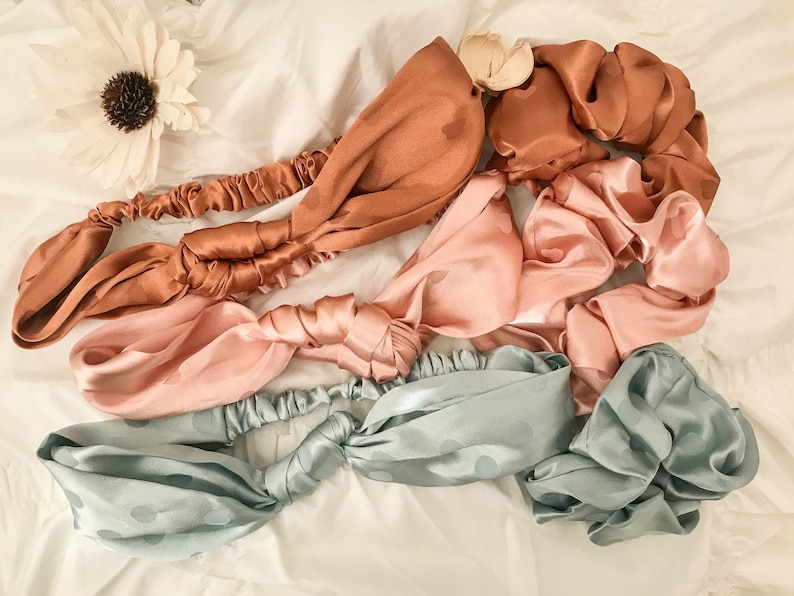 May include: Four satin headbands in different colors and patterns. The headbands are tied in a knot and are lying on a white surface. The headbands are in the colors of light blue, pink, and brown.