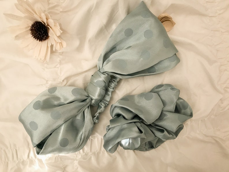 May include: Two sage green satin hair scrunchies with white polka dots. One scrunchie is tied in a bow shape, the other is a simple scrunchie.