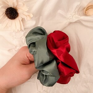 May include: Two scrunchies, one green and one red, made of satin fabric. The scrunchies are tied together and held in a hand.