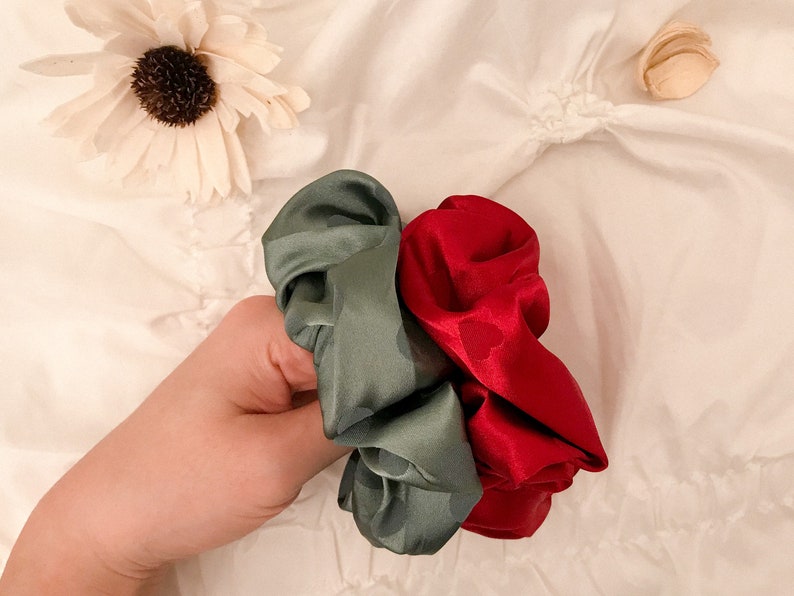 May include: Two scrunchies, one green and one red, made of satin fabric. The scrunchies are tied together and held in a hand.