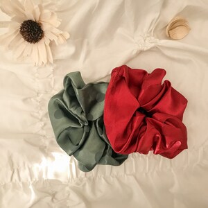 May include: Two fabric hair scrunchies, one green with white polka dots and one red. The scrunchies are on a white fabric background.