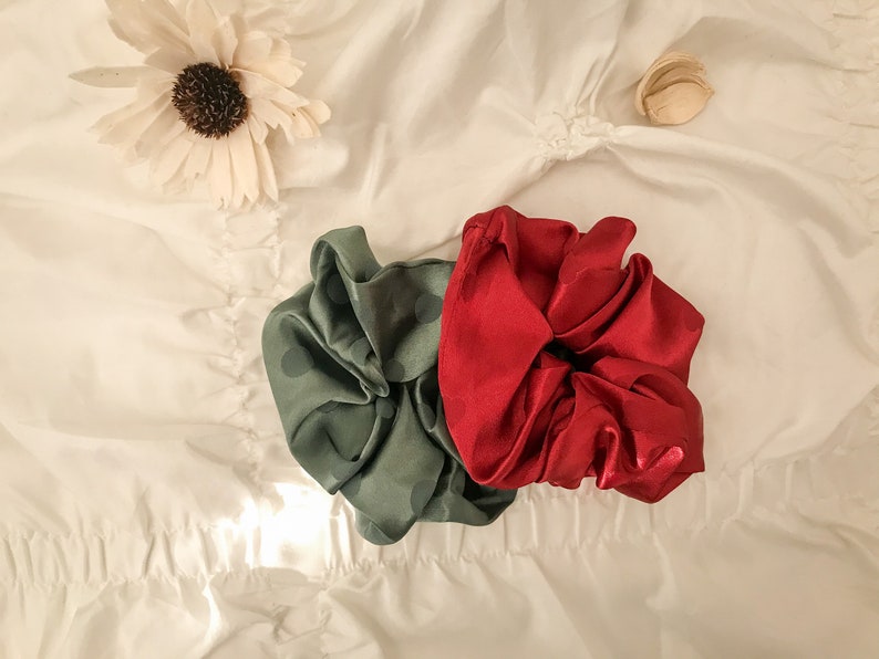 May include: Two fabric hair scrunchies, one green with white polka dots and one red. The scrunchies are on a white fabric background.
