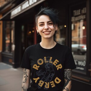 Op de afbeelding: Een persoon draagt een zwart T-shirt met een gele afbeelding van een roller derby-speler. De afbeelding zegt "Roller Derby" en "Revival" in een vintage lettertype.