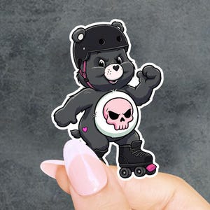 May include: A die-cut sticker featuring a dark gray cartoon bear wearing a black helmet and black roller skates. The bear has a white belly patch with a pink skull graphic, a small pink heart on its hip, and a determined expression.