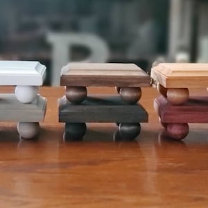 May include: Four wooden tiered stands with rounded legs. The stands are painted in different colors: white, gray, brown, and red.