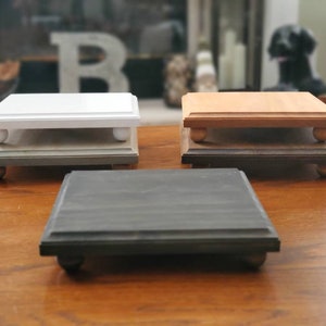 May include: Three wooden tiered display stands with rounded edges. The top tier is white, the middle tier is brown, and the bottom tier is black. Each tier has four small wooden feet.