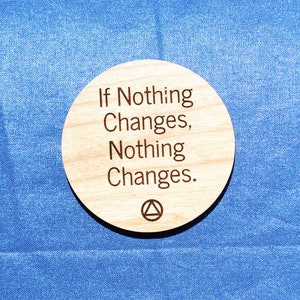 May include: A round wooden coaster with the text "If Nothing Changes, Nothing Changes." The coaster is on a blue surface.