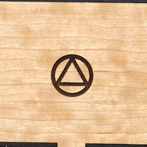 May include: A wooden box with a black border and a triangle inside a circle design on the front.