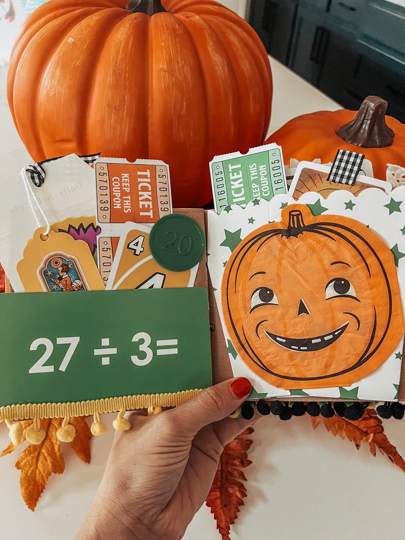 May include: A decorative scrapbook page featuring a green card with the text 27 &divide; 3=, a round green token with the number 20, orange and green admission tickets, a playing card with the number 4, and a cutout of a smiling jack-o'-lantern.