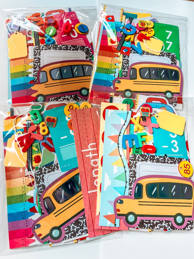 May include: Four clear plastic bags filled with colorful school-themed craft supplies. The bags contain items like stickers, paper, and cutouts of school buses, crayons, and numbers. The bags are labeled with the words "Grade", "Math", and "77".