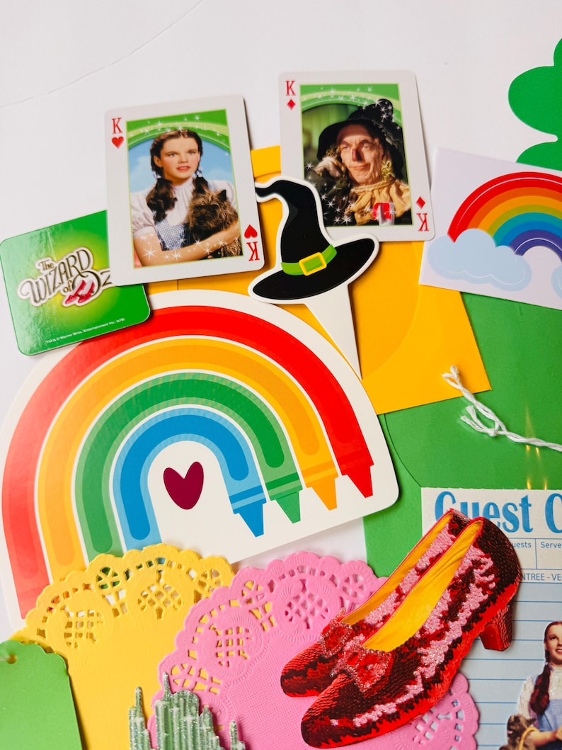 May include: A selection of Wizard of Oz themed items. Features playing cards with character portraits, a black witch's hat, a rainbow, a pair of red sequined shoes, and a green sign with the text "The Wizard of Oz".