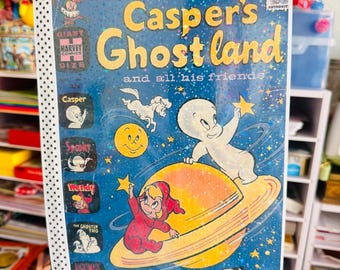 Może przedstawiać: Komiks Casper's Ghostland and all his friends z niebieskim tłem kosmicznym, przedstawiający przyjaznego duszka Kacpra, żółtą planetę z pierścieniami oraz inne postacie. Okładka zawiera logo Harvey Comics oraz napisy.