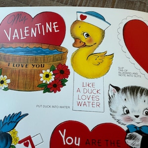 May include: A sheet of vintage Valentine's Day cutouts. Designs include a red heart with "My Valentine" text, a yellow duck in a sailor hat, and two kittens. Other elements include a wooden tub with "I Love You" text and flowers.