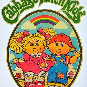 May include: A vintage Cabbage Patch Kids graphic featuring two cartoon children within a circular frame. The girl wears a pink dress and the boy wears blue overalls. A rainbow and the words "Cabbage Patch Kids" are also in the image.