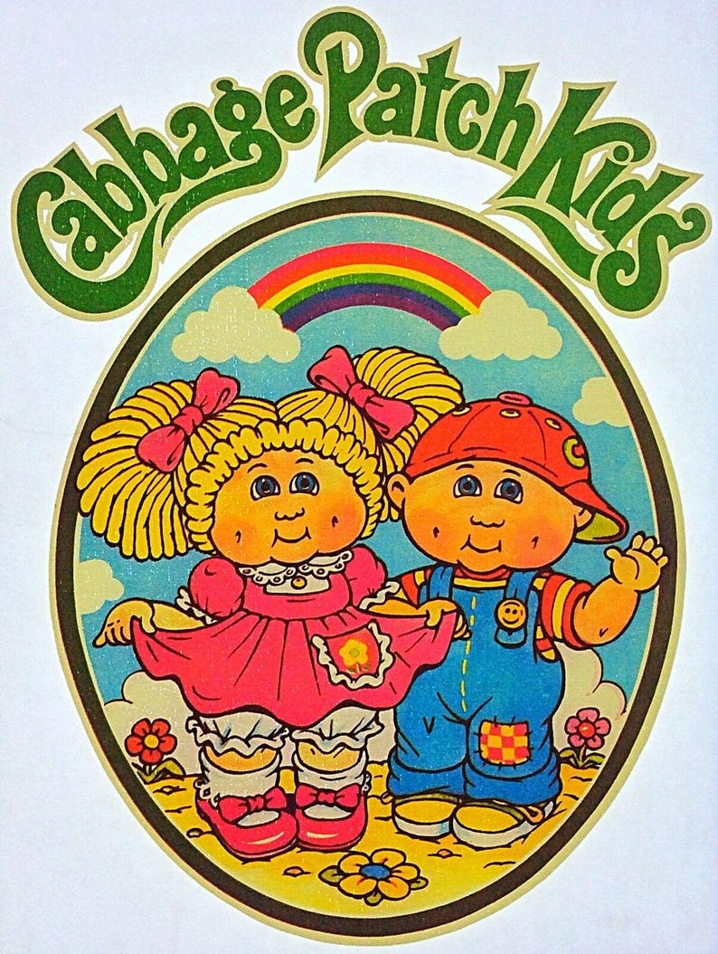 May include: A vintage Cabbage Patch Kids graphic featuring two cartoon children within a circular frame. The girl wears a pink dress and the boy wears blue overalls. A rainbow and the words "Cabbage Patch Kids" are also in the image.