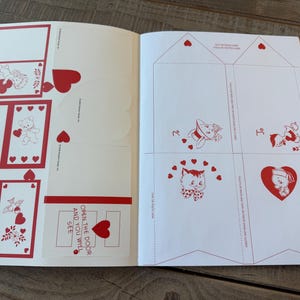 May include: Open book with Valentine's Day themed cutouts and illustrations. The pages feature red and white designs, including hearts, teddy bears, and a cat. Text on the page reads "Open the door and you will see."