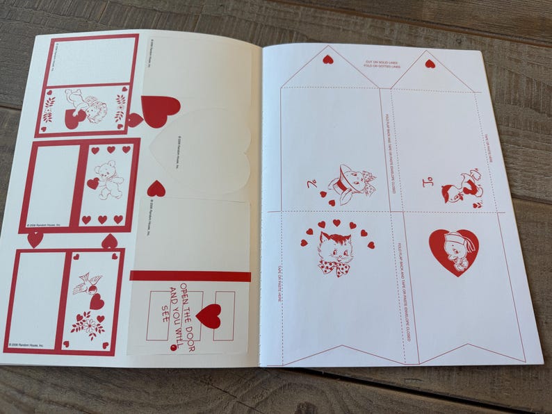 May include: Open book with Valentine's Day themed cutouts and illustrations. The pages feature red and white designs, including hearts, teddy bears, and a cat. Text on the page reads "Open the door and you will see."