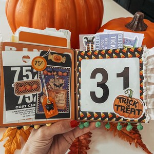 May include: A Halloween-themed scrapbook page featuring a black and white bingo card, a vintage-style illustration of a witch, a black cat charm, and a large number 31. The page is decorated with candy corn patterns and a Trick or Treat pumpkin sticker.