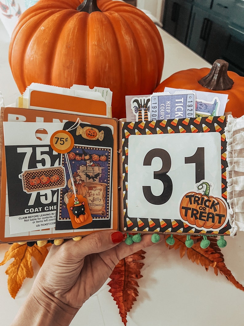 May include: A Halloween-themed scrapbook page featuring a black and white bingo card, a vintage-style illustration of a witch, a black cat charm, and a large number 31. The page is decorated with candy corn patterns and a Trick or Treat pumpkin sticker.