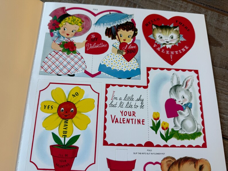 May include: A selection of vintage Valentine's Day cutouts. The illustrations include children, a cat, and a bunny, all holding hearts. Text includes "To My Valentine" and "I love you". A flower cutout offers "Yes", "Maybe", and "No" options.