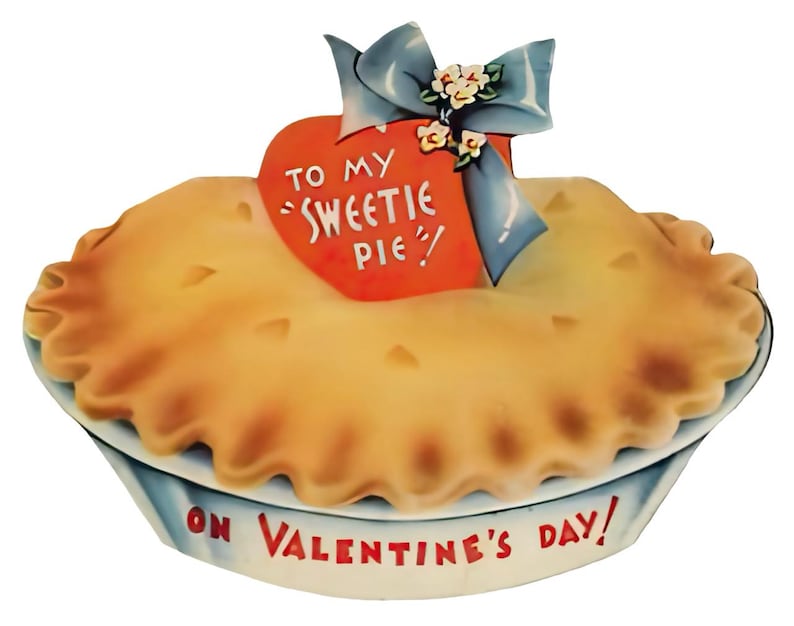 May include: A vintage Valentine's Day card in the shape of a pie. The pie has a golden-brown crust and sits in a white and blue dish. A red heart with the words "TO MY 'SWEETIE PIE'" is attached to the pie with a blue bow and small flowers. The words "ON VALENTINE'S DAY!" are written on the dish.