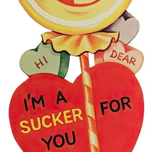 May include: A retro Valentine's Day lollipop decoration. The lollipop features a smiling face and the text "I'M A SUCKER FOR YOU". Heart-shaped candies say "HI", "DEAR", "BE MINE", and "LOVE".