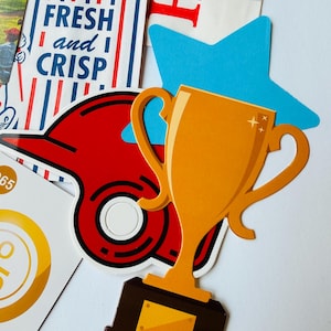 Op de afbeelding: Een verzameling stickers met een gouden trofee, een rode honkbalpet, een blauwe ster en een rechthoekige kaart met blauwe strepen en de tekst FRESH and CRISP. De stickers zijn in een gelaagde compositie op een witte ondergrond geplaatst.