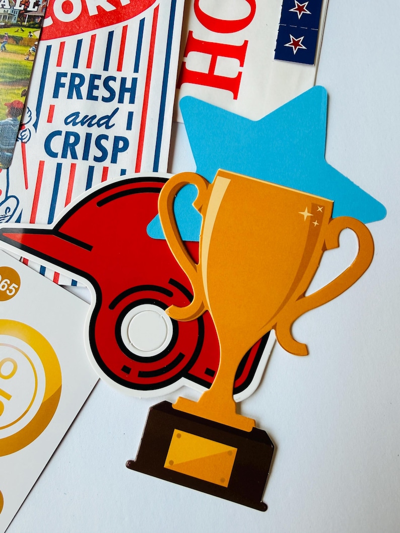 Op de afbeelding: Een verzameling stickers met een gouden trofee, een rode honkbalpet, een blauwe ster en een rechthoekige kaart met blauwe strepen en de tekst FRESH and CRISP. De stickers zijn in een gelaagde compositie op een witte ondergrond geplaatst.