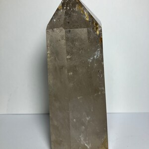 May include: A large, clear quartz crystal point with a smoky brown hue and inclusions. The crystal is faceted and has a pointed tip.
