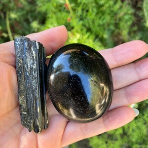 May include: A black obsidian palm stone and a black tourmaline crystal cluster. The crystals are smooth and polished.