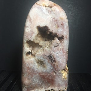 May include: A large, freeform, pink and white geode with a natural, rough exterior and a hollow interior lined with white crystals. The geode has a brown and white pattern on the exterior.