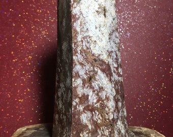 May include: A red and white crystal point with a rough, natural texture. The point is sitting on a piece of petrified wood.