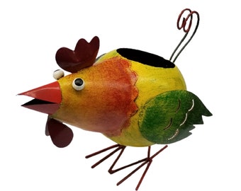 May include: A colorful metal chicken planter with a yellow body, red and orange accents, and green wing details. The chicken has a red beak and comb, with black legs and a curly tail. The planter has a black opening for plants.