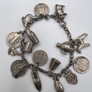 Peut inclure: Un bracelet de charme argenté vintage orné de divers breloques, dont des pièces de monnaie, un cochon, une chaussure, un dé à coudre et un shaker à cocktails. Le bracelet est fait d'une chaîne.