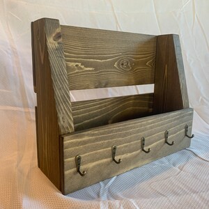 May include: A rustic wooden wall organiser with a shelf and five hooks. The organiser is stained a dark brown colour and has a natural wood grain.