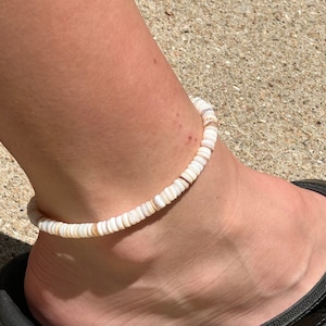 Könnte beinhalten: Ein schlichtes Fußkettchen aus weißen Muscheln. Das Fußkettchen besteht aus kleinen, runden Muscheln, die auf einer dünnen Schnur aufgefädelt sind.