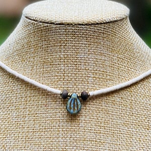 May include: A white beaded choker necklace with a blue and white ceramic pendant shaped like a teardrop. The pendant has a decorative pattern.