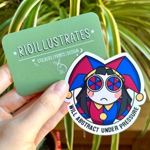 Può includere: Un adesivo raffigurante un giullare dei cartoni animati con una combinazione di colori rosso, blu e giallo. Il testo "WILL ABSTRACT UNDER PRESSURE" è sull'adesivo. È visibile anche una carta verde con la scritta "RIOILLUSTRATES".