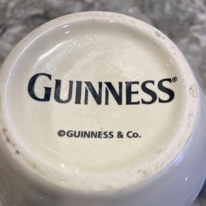 May include: White ceramic mug with the word "GUINNESS" in black lettering and the copyright symbol followed by "GUINNESS & Co."
