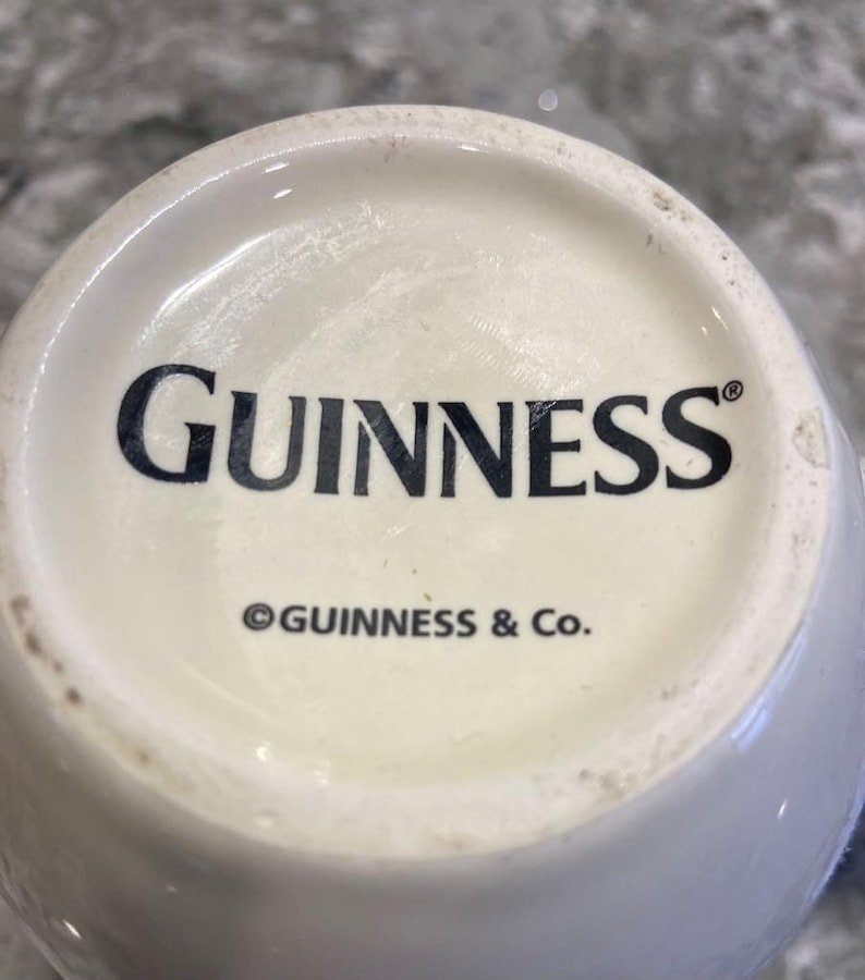 May include: White ceramic mug with the word "GUINNESS" in black lettering and the copyright symbol followed by "GUINNESS & Co."